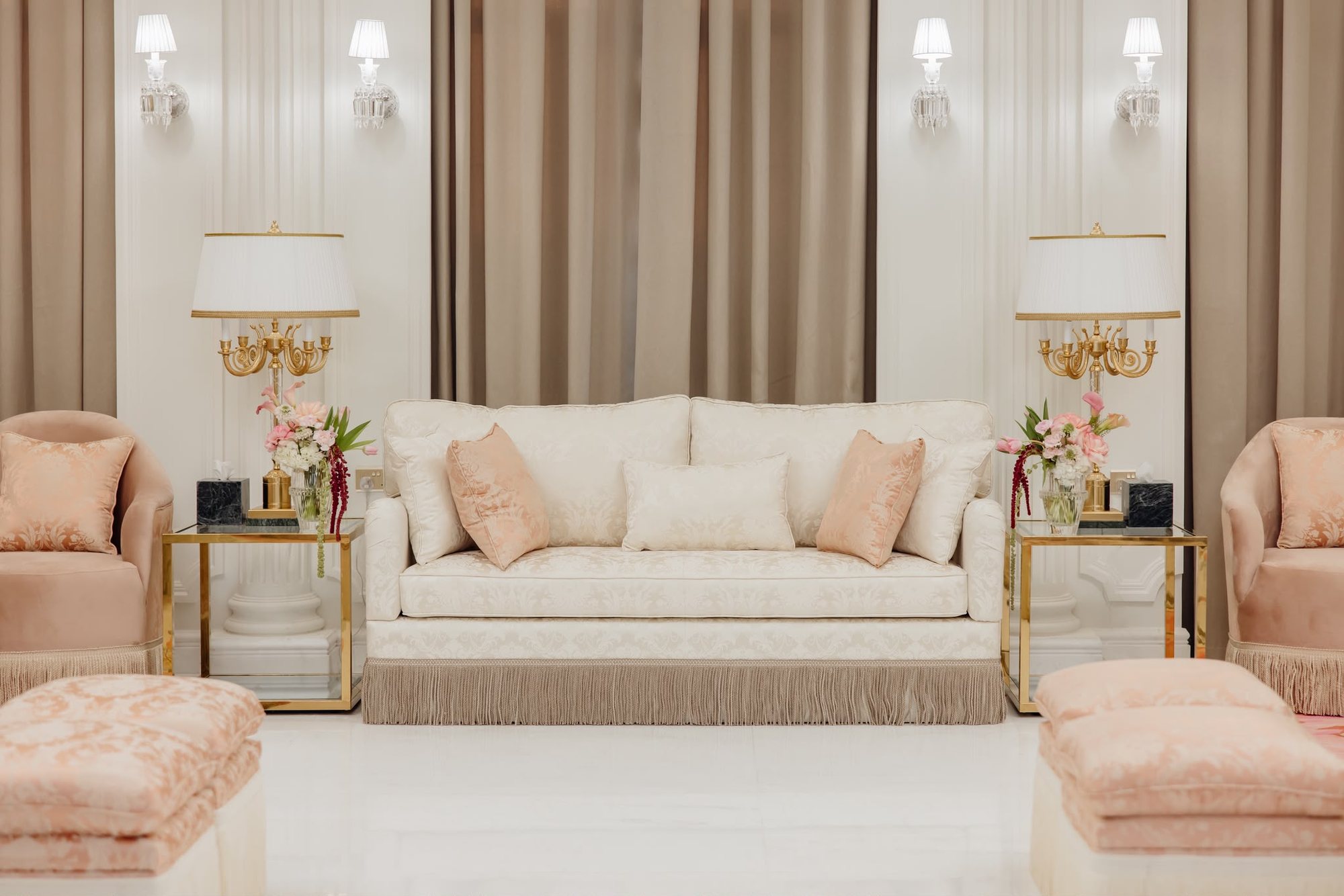 Frontal real project seating wall with cream sofa, blush chairs, brass lamps, taupe curtains, and wall sconces