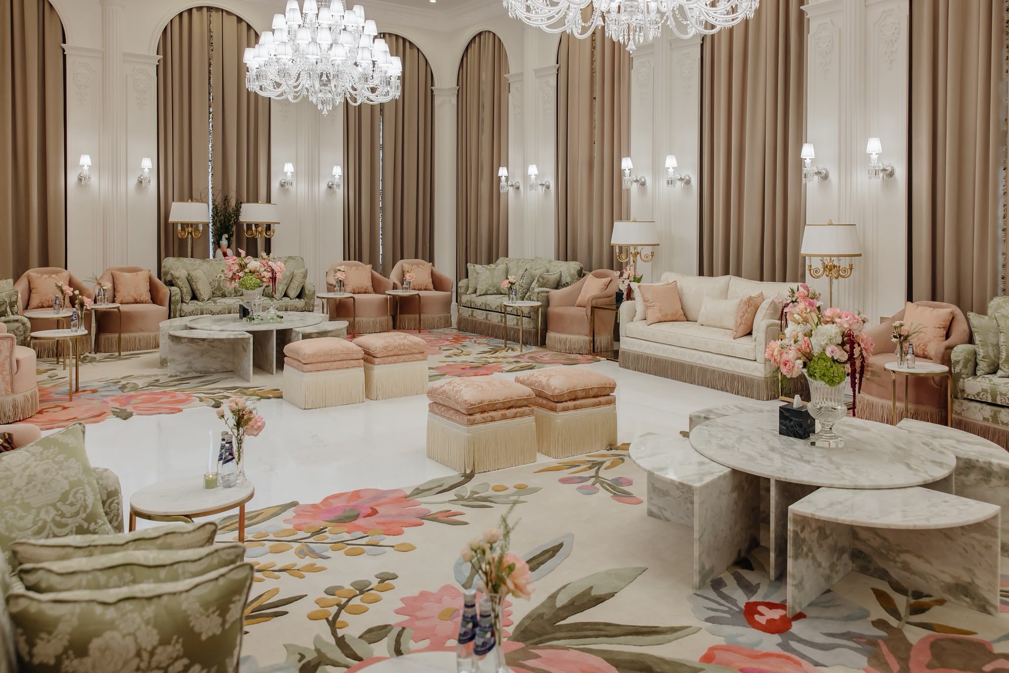Wide real project majlis with crystal chandelier, sage seating, blush chairs, cream sofas, floral rug, and marble tables