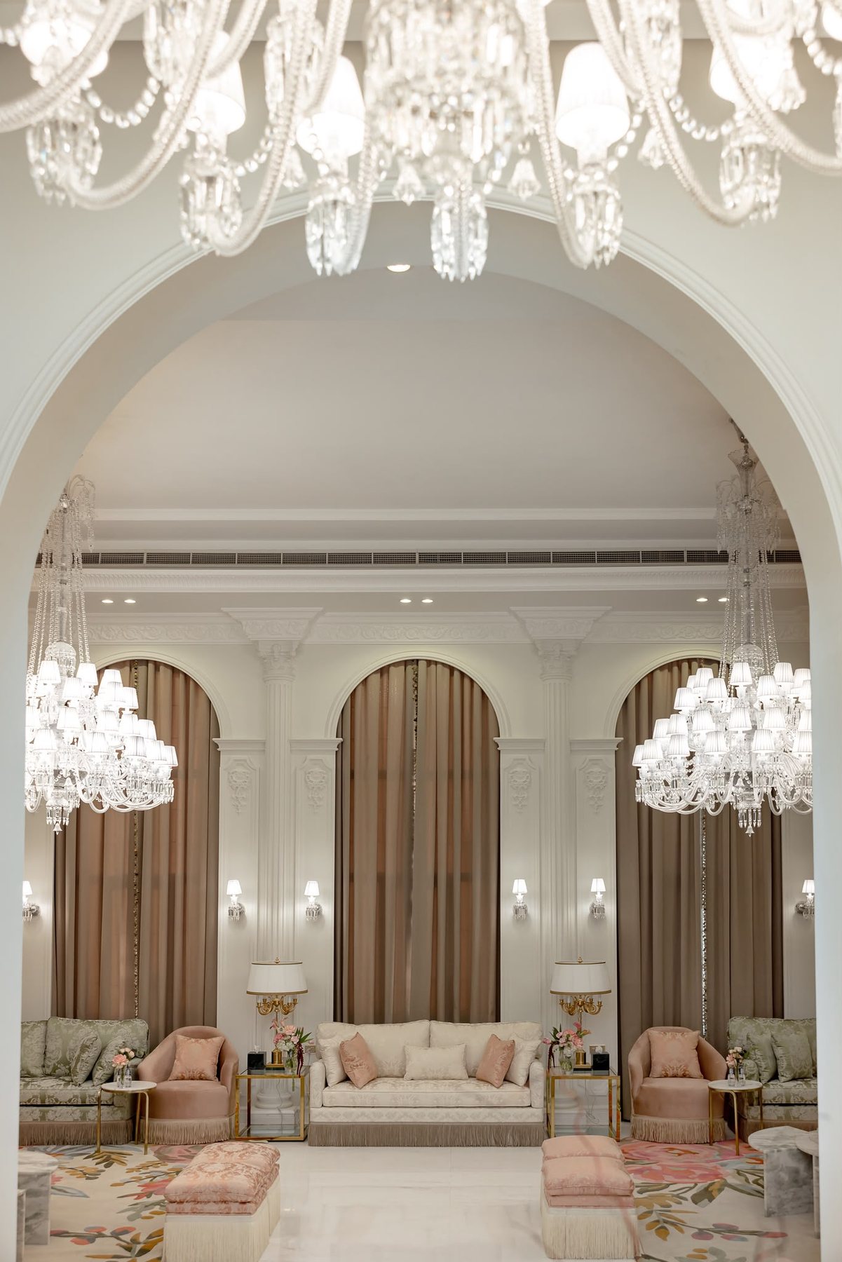 Vertical real project arch view with chandeliers, marble table, cream sofa, and blush seating