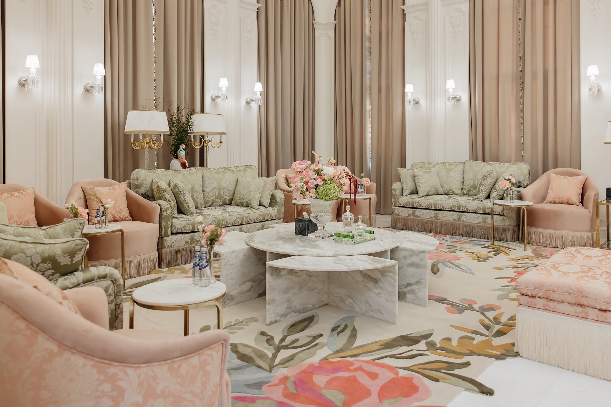 Angled real project sitting area with marble tables, sage upholstery, blush chairs, taupe curtains, and lamps
