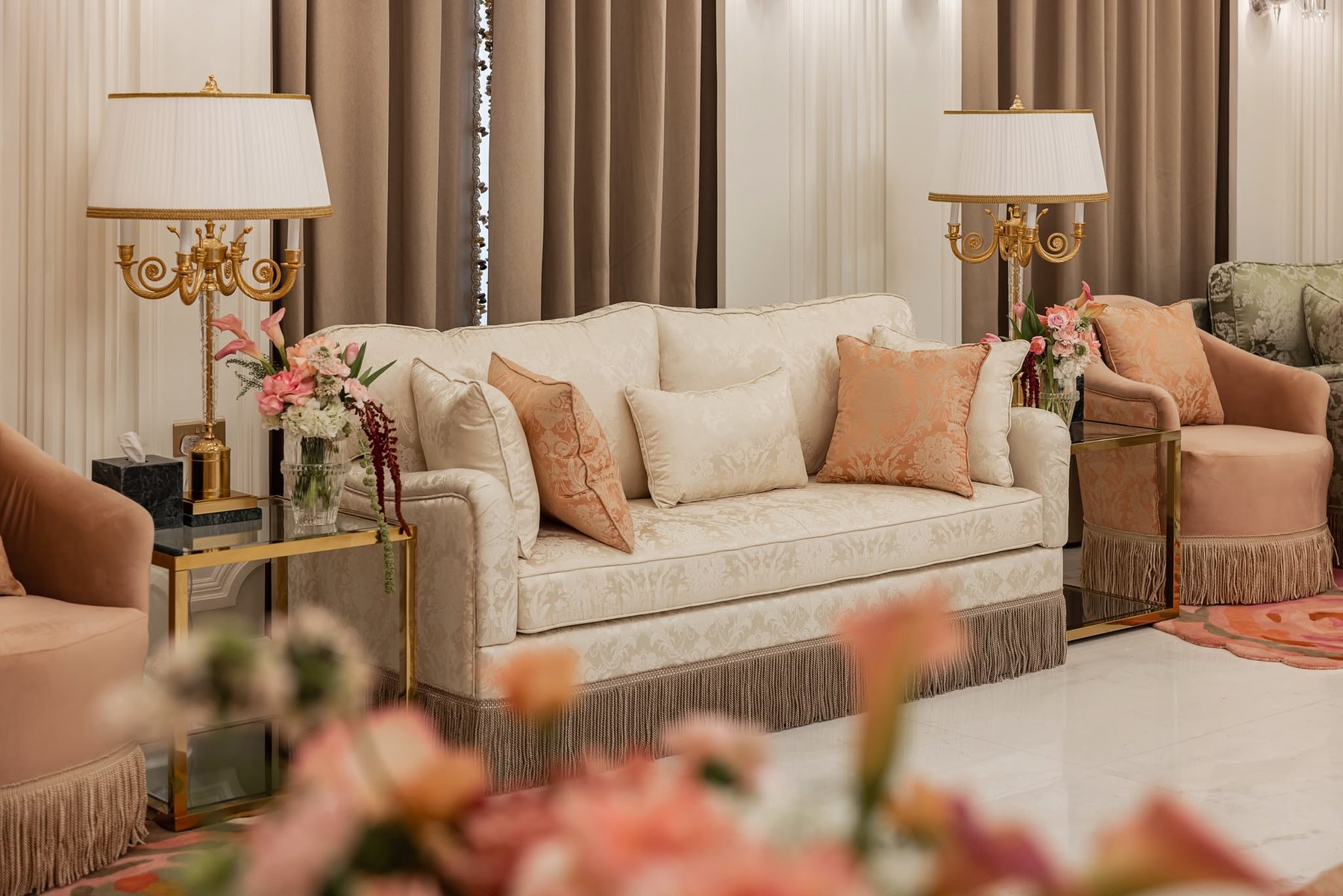 Real project close room angle with cream sofa, blush cushions, side lamps, champagne accents, and taupe curtains